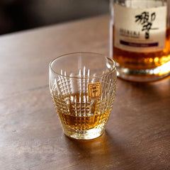 Amber drink in a Kohaku Nanako glass on a wood table with a whiskey bottle behind it