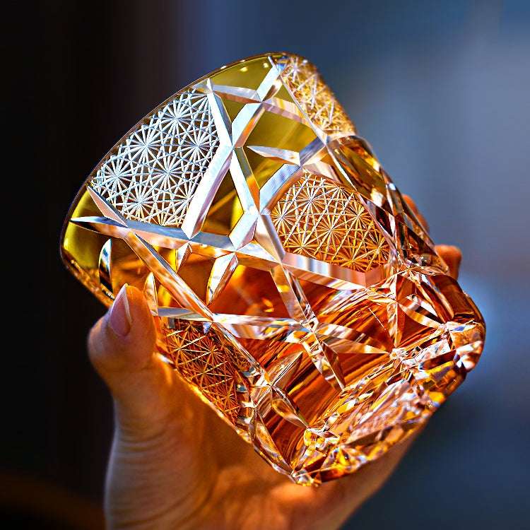 Amber hand-cut whisky glass held up to the light, its honey-coloured body divided into diagonal panels of fine starburst cutting