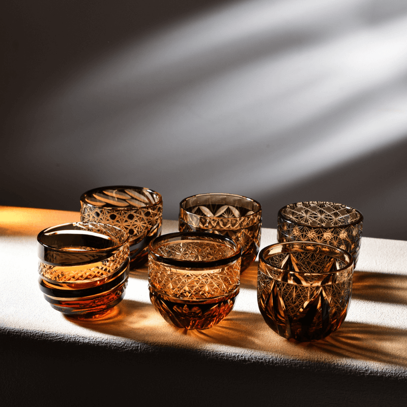 Six amber Edo Kiriko sake cups in a row, each cut in a different traditional pattern