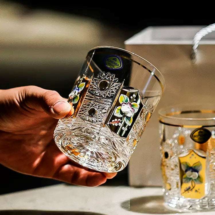 A pair of enamel-painted crystal glasses, one held in the hand beside its gift box