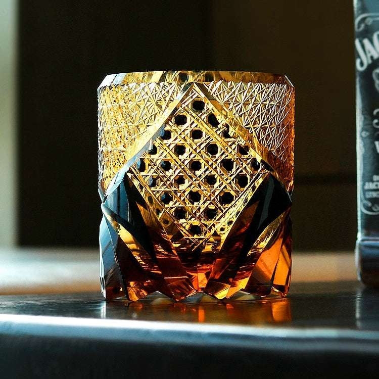 Amber Edo Kiriko whisky glass on a bar top beside a bottle, lattice and starburst cutting lit from the side