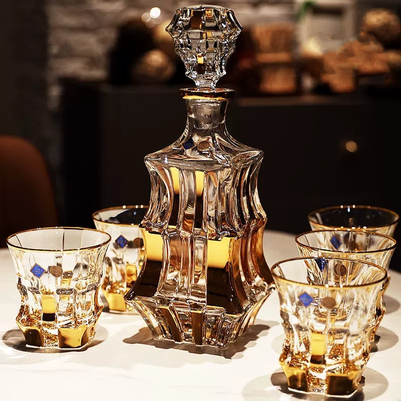 A gold-banded crystal decanter with four matching glasses set out on a table