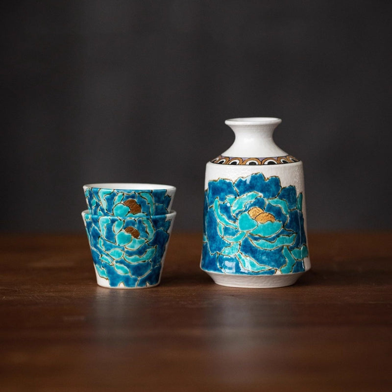Kutani porcelain sake set: a white flagon and two stacked cups hand-painted with blue and teal peonies outlined in gold