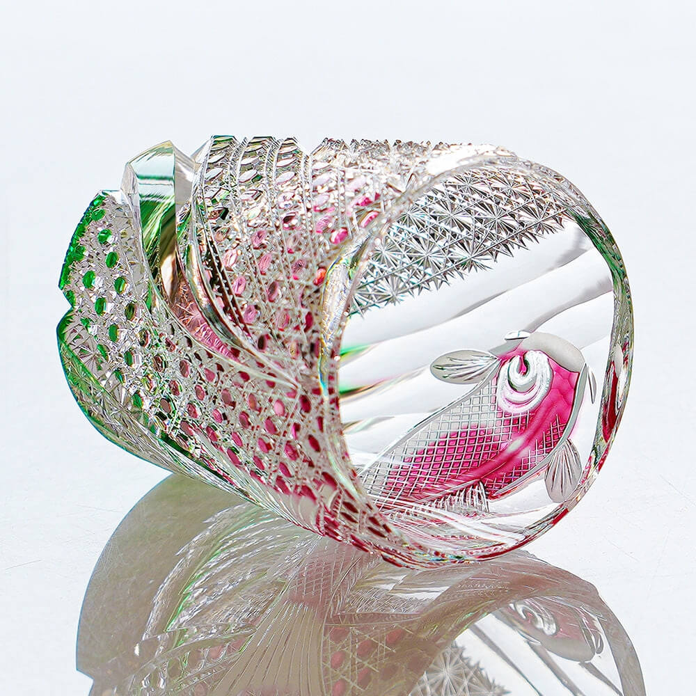 Edo Kiriko Kingyo Nishiki whisky glass lying down with pink fish motif on reflective surface