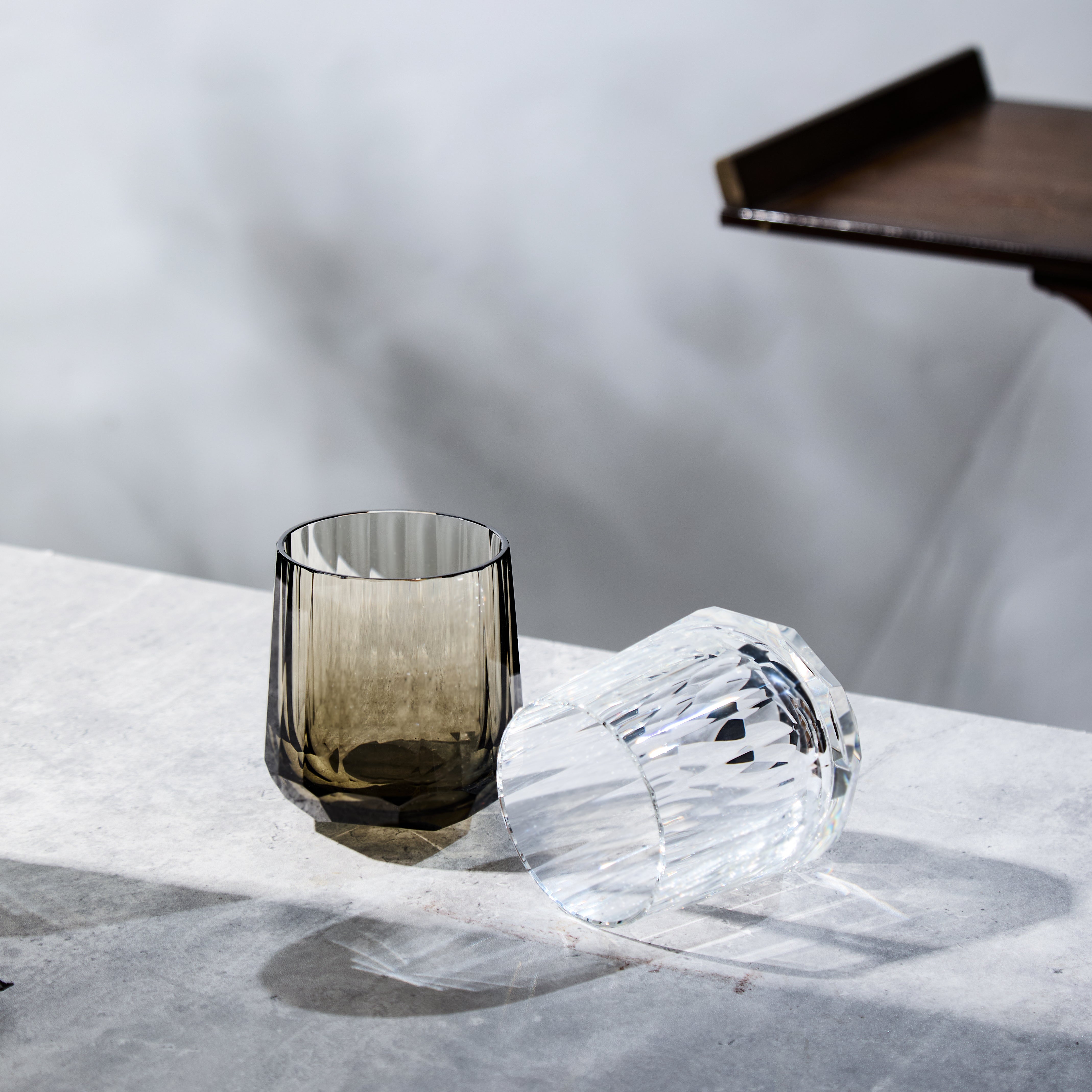 Clear and smoky Edo Kiriko Kage-Tate whisky glasses on stone surface with soft reflections
