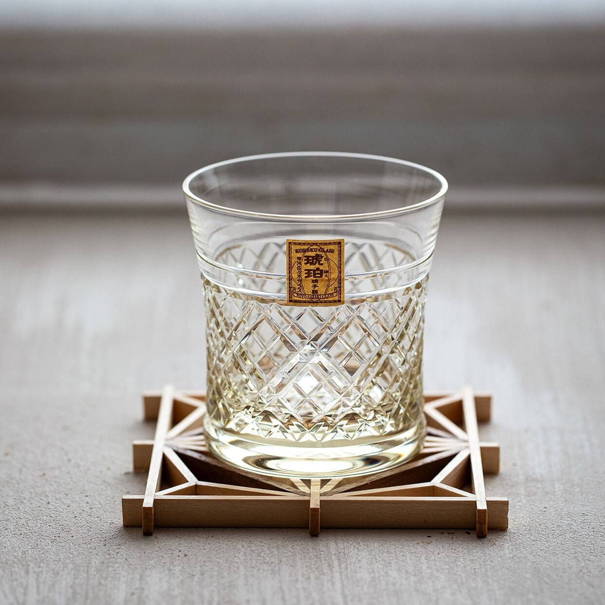 Empty Kohaku Kagome glass with crossed lattice cutting on a geometric wooden coaster