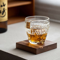 Amber drink in a Kohaku Kiku glass with fan and floral cuts on a square wooden coaster