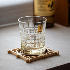 Empty Kohaku Kiku glass with fan-shaped cuts resting on a geometric wooden coaster