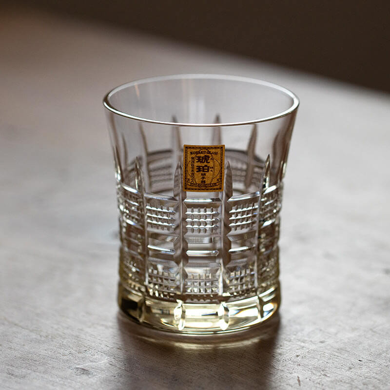 Empty Kohaku Yarai glass on a pale surface, showing vertical lines and square lattice cuts