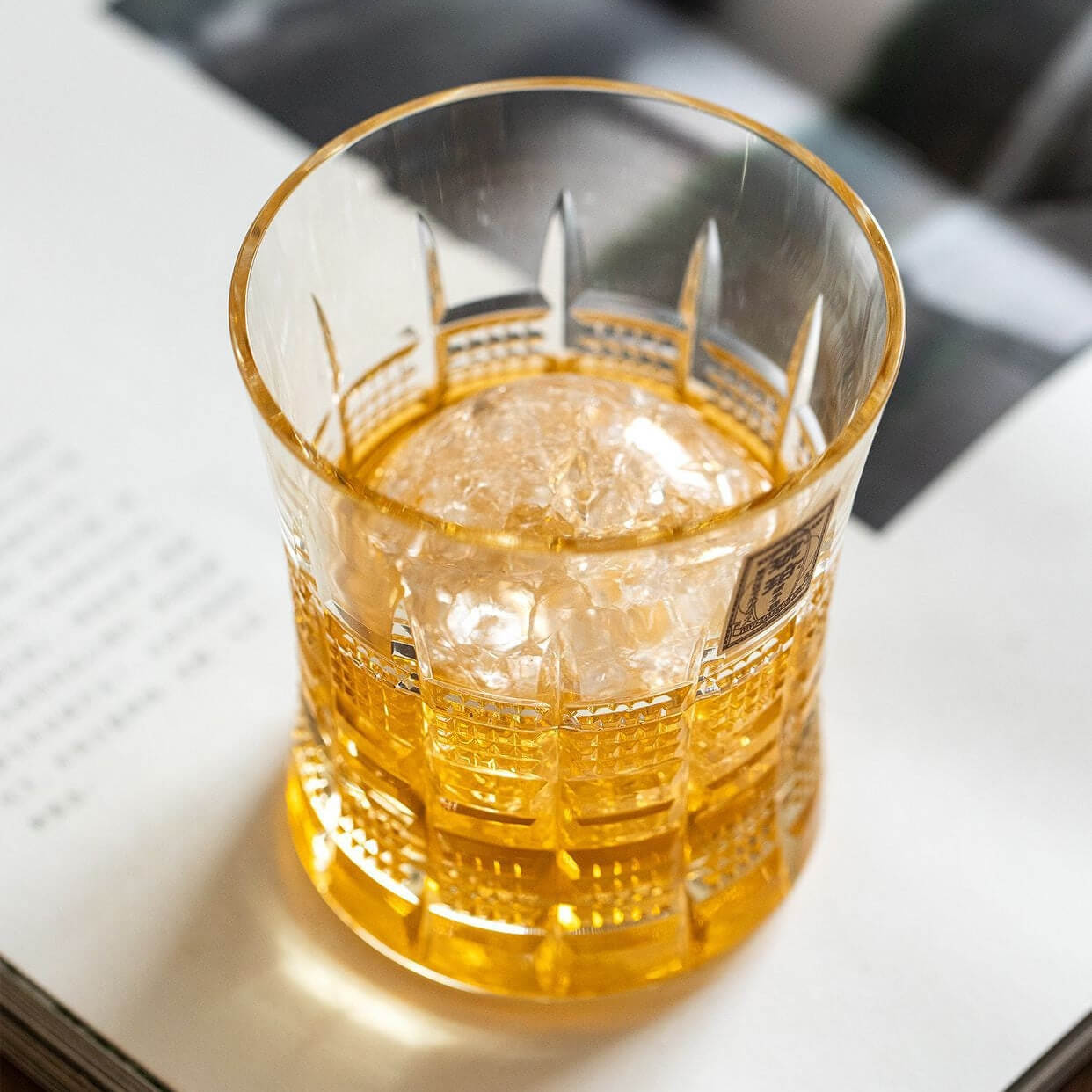 Top view of an amber drink with ice in a Kohaku Yarai glass on an open book